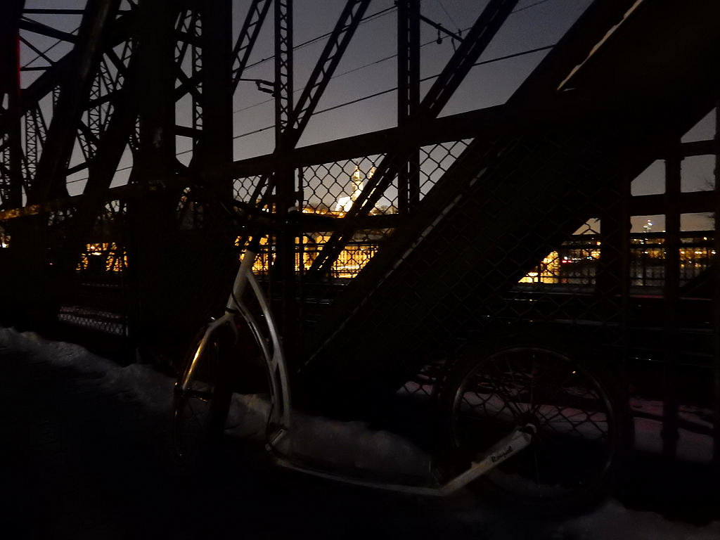 Vyšehrad svítí na skále nad Vltavou. Koloběžka odpočívá na Železničním mostě.