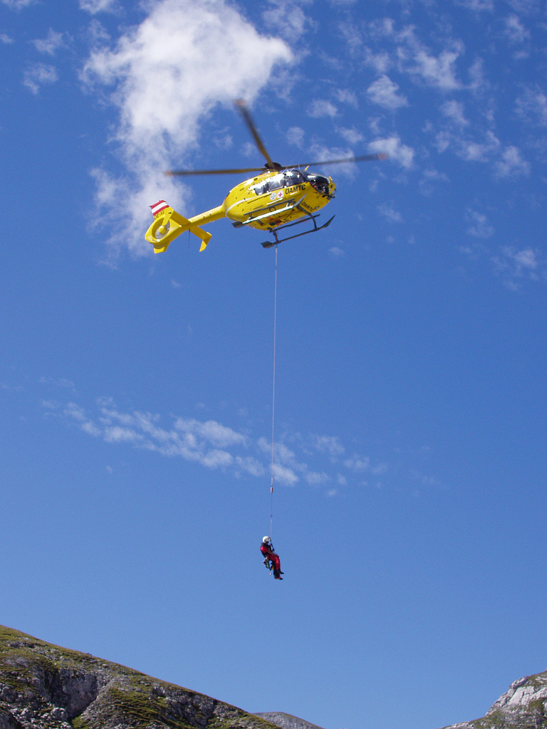 Záchranář visí pod vrtulníkem, který ho dopravuje ke skalní stěně Hochthron. 
