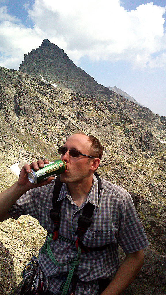 Geo pije vrcholové pivo na Žabím koni ve Vysokých Tatrách. Vzadu se tyčí Český / Ťažký štít - zleva na něj vede hřeben od Váhy a zprava přes Kohútik.
