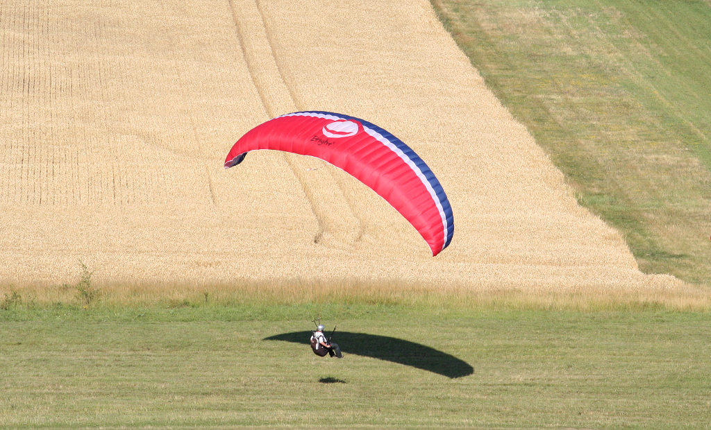 Paraglider přistává na rozhraní louky a pole.
