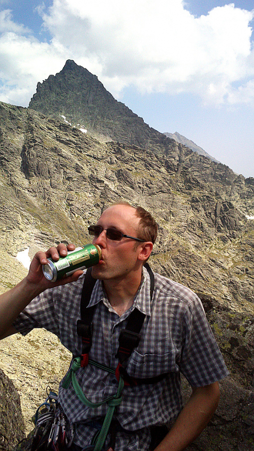 Geo pije vrcholové pivo na Žabím koni ve Vysokých Tatrách. Vzadu se tyčí Český / Ťažký štít - zleva na něj vede hřeben od Váhy a zprava přes Kohútik.